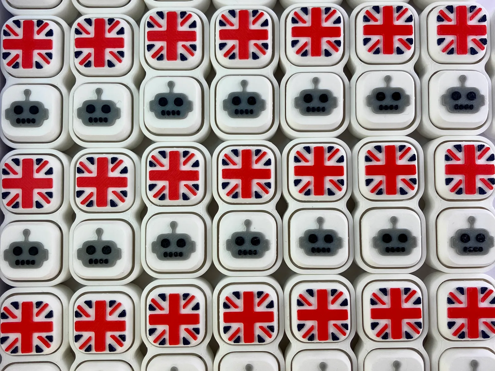 A tray of white Twin clickers in neat rows, alternating robot caps and Union Jack caps